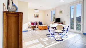 A spacious living room with a sofa, chairs, a TV, and a balcony with a view.