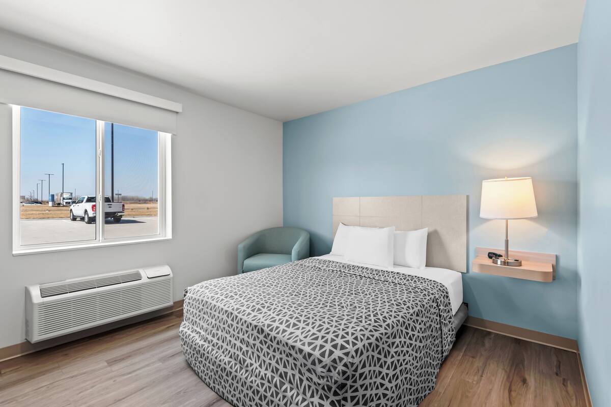 Een hotelkamer met een bed, een stoel, een nachtkastje met een lamp, een raam met uitzicht en een wandradiator.