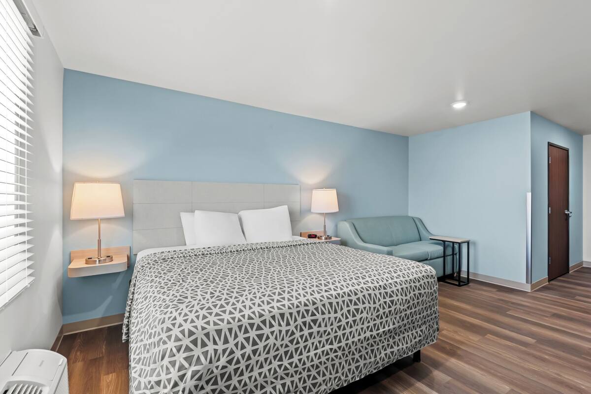 Een hotelkamer met een bed, twee nachtkastjes met lampen, een stoel en een deur.