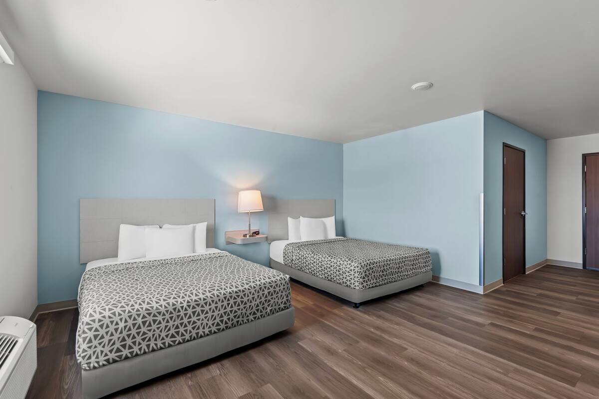 Een hotelkamer met twee bedden, een nachtkastje met een lamp en een houten vloer.