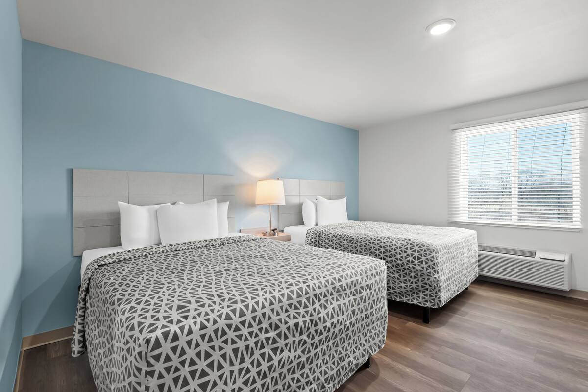 Een hotelkamer met twee bedden, een nachtkastje, een lamp en een raam met luxaflex.