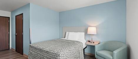 A hotel room with a bed, a nightstand with a lamp, a chair, and a door.