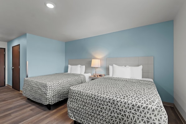 A hotel room with two beds, a nightstand with a lamp, and a wooden floor. - Woodspring Suites Coralville Iowa City (Coralville)