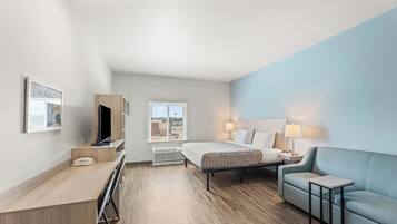 A modern hotel room with a bed, a desk, a chair, and a TV.
