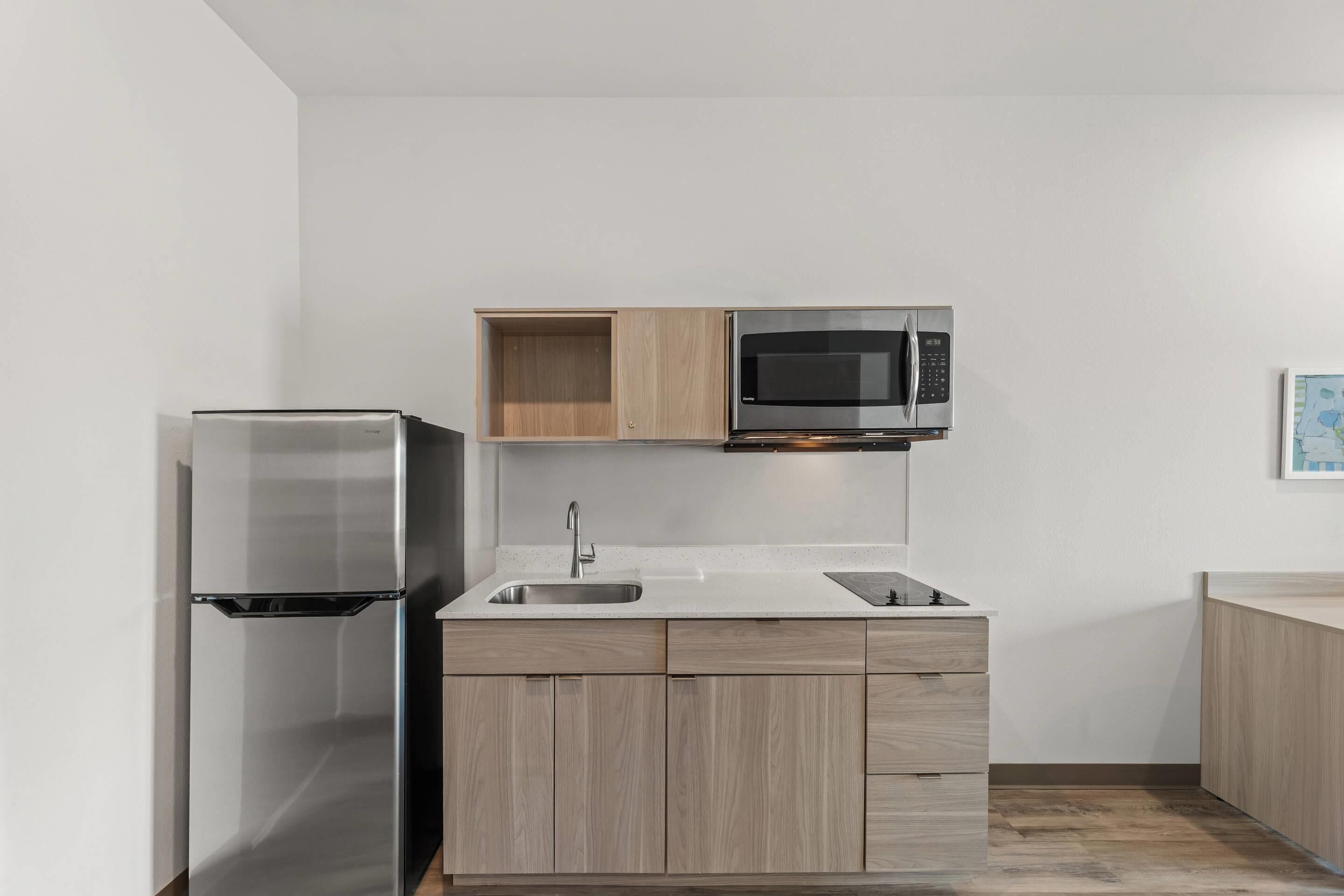 A modern kitchen with a stainless steel refrigerator, a microwave, and wooden cabinets.