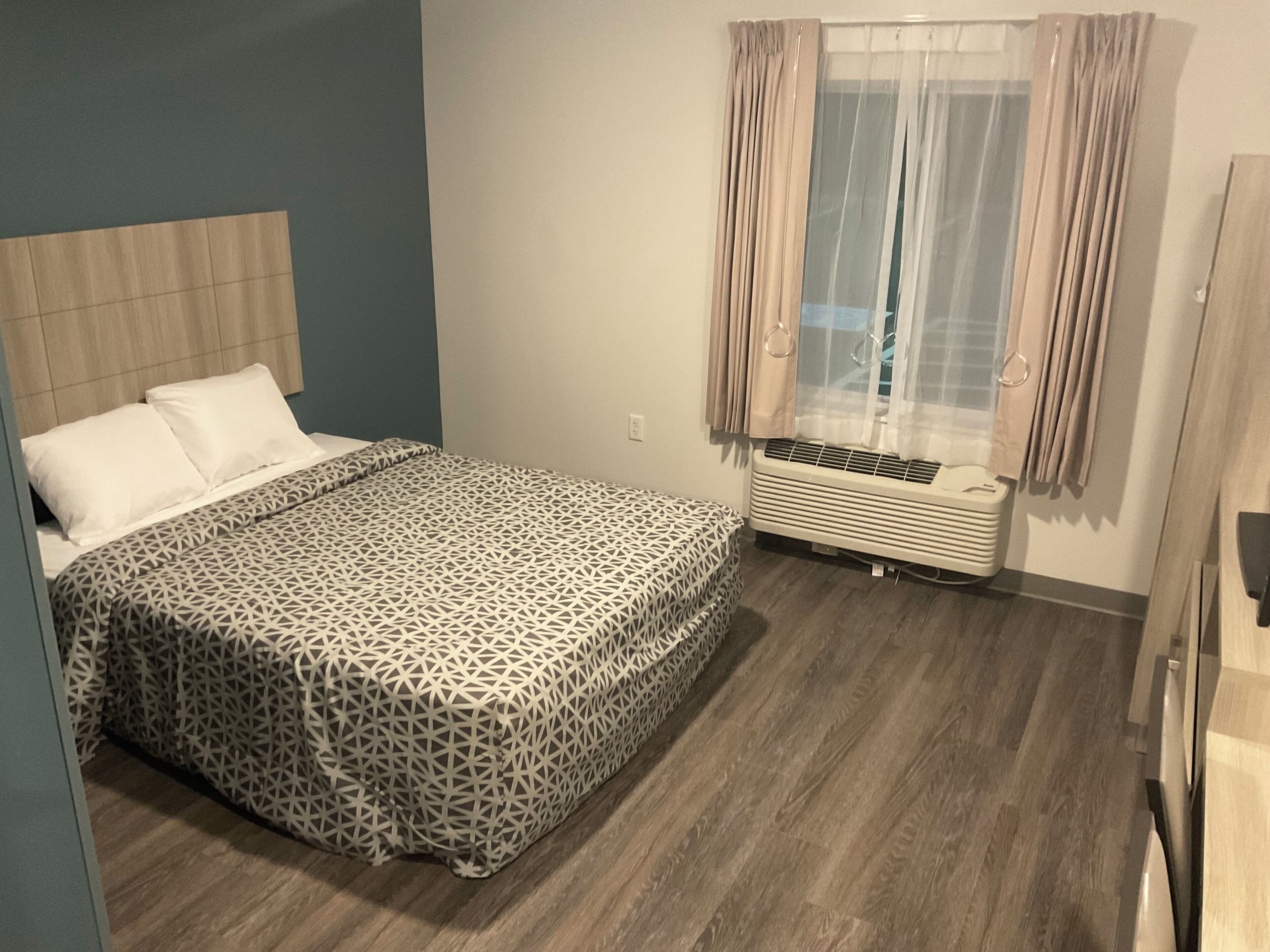 A bedroom with a bed, a window with curtains, a heater, and a wooden floor.