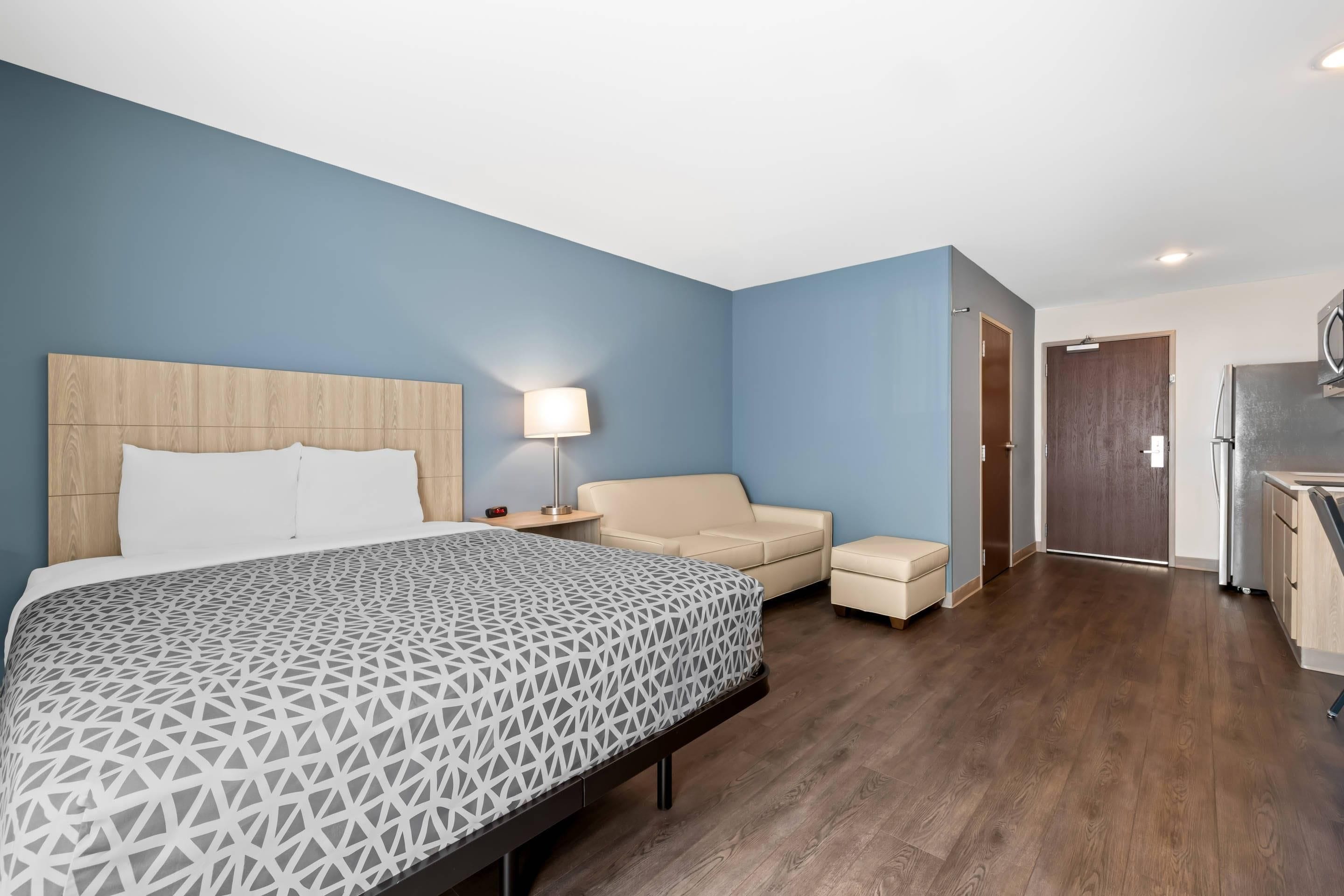 Habitación de hotel con cama, mesita de noche, lámpara, sofá y kitchenette.