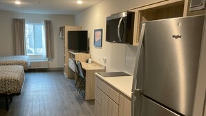 A modern kitchen with a refrigerator, microwave, and a flat-screen TV. There is a wooden desk and a chair, and a window with curtains. - Woodspring Suites Charlotte Airport (Charlotte)