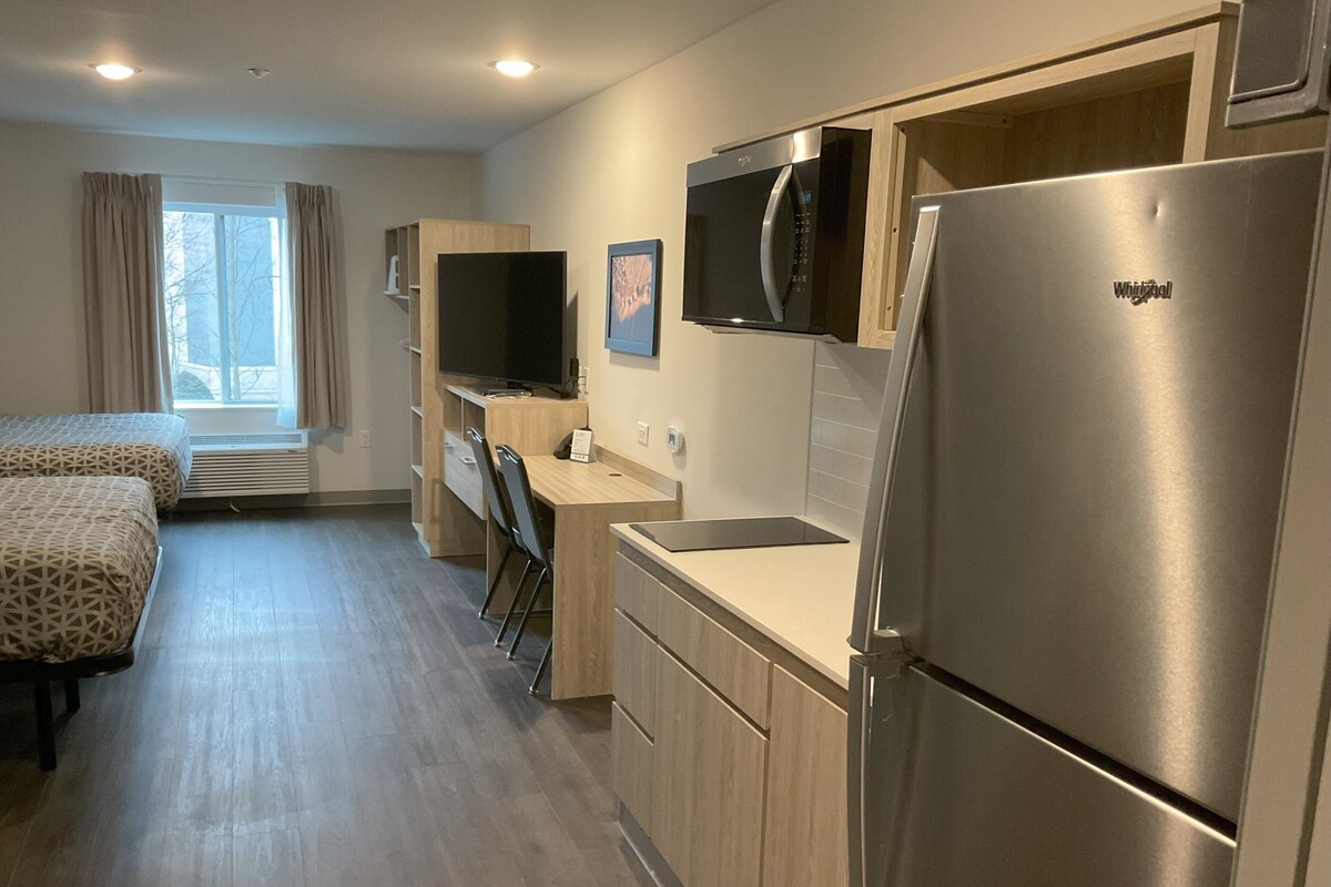 Una cocina moderna con refrigerador, microondas y televisor de pantalla plana. Incluye un escritorio de madera y una silla, además de una ventana con cortinas.
