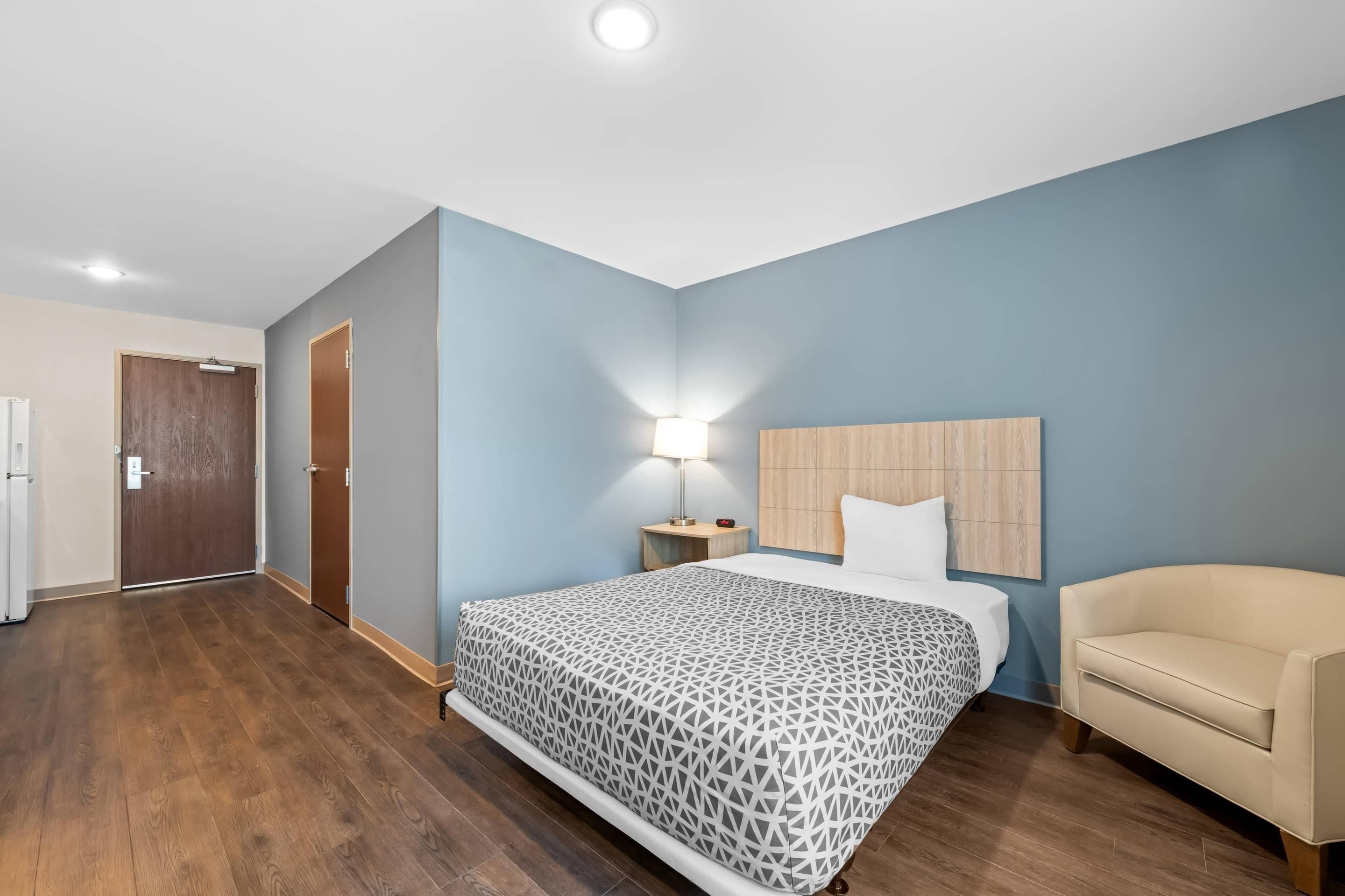 Una habitación de hotel con una cama, una mesita de noche, una lámpara, una silla y una puerta.