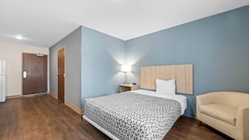 Una habitación de hotel con una cama, una mesita de noche, una lámpara, una silla y una puerta.
