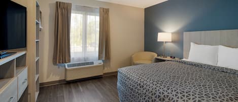A hotel room with a bed, a desk, a chair, a TV, a lamp, and a window with curtains.