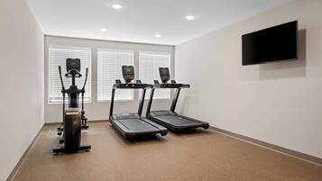 Un gimnasio con tres cintas de correr, una bicicleta estática y un televisor montado en la pared.