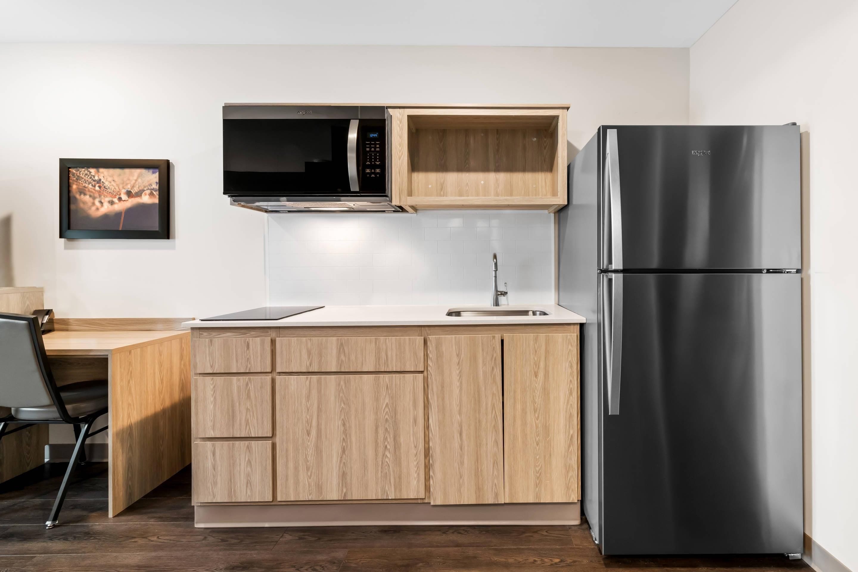 A compact kitchen with a built-in microwave, a stainless steel refrigerator, and wooden cabinetry.
