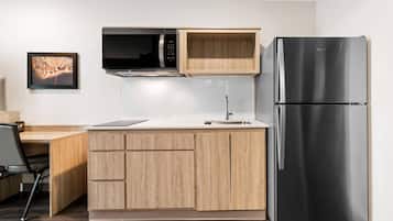 Cocina compacta con microondas integrado, refrigerador de acero inoxidable y armarios de madera.