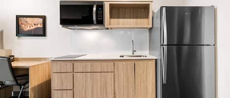 A compact kitchen with a built-in microwave, a stainless steel refrigerator, and wooden cabinetry.