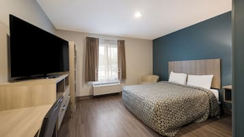 Ein modernes Hotelzimmer mit Flachbildfernseher, einem Bett mit gemusterten Bettwäsche, einem Schreibtisch mit Stuhl und einem Fenster mit Vorhängen.