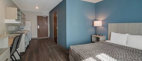 A hotel room with a bed, a desk, and a kitchenette.