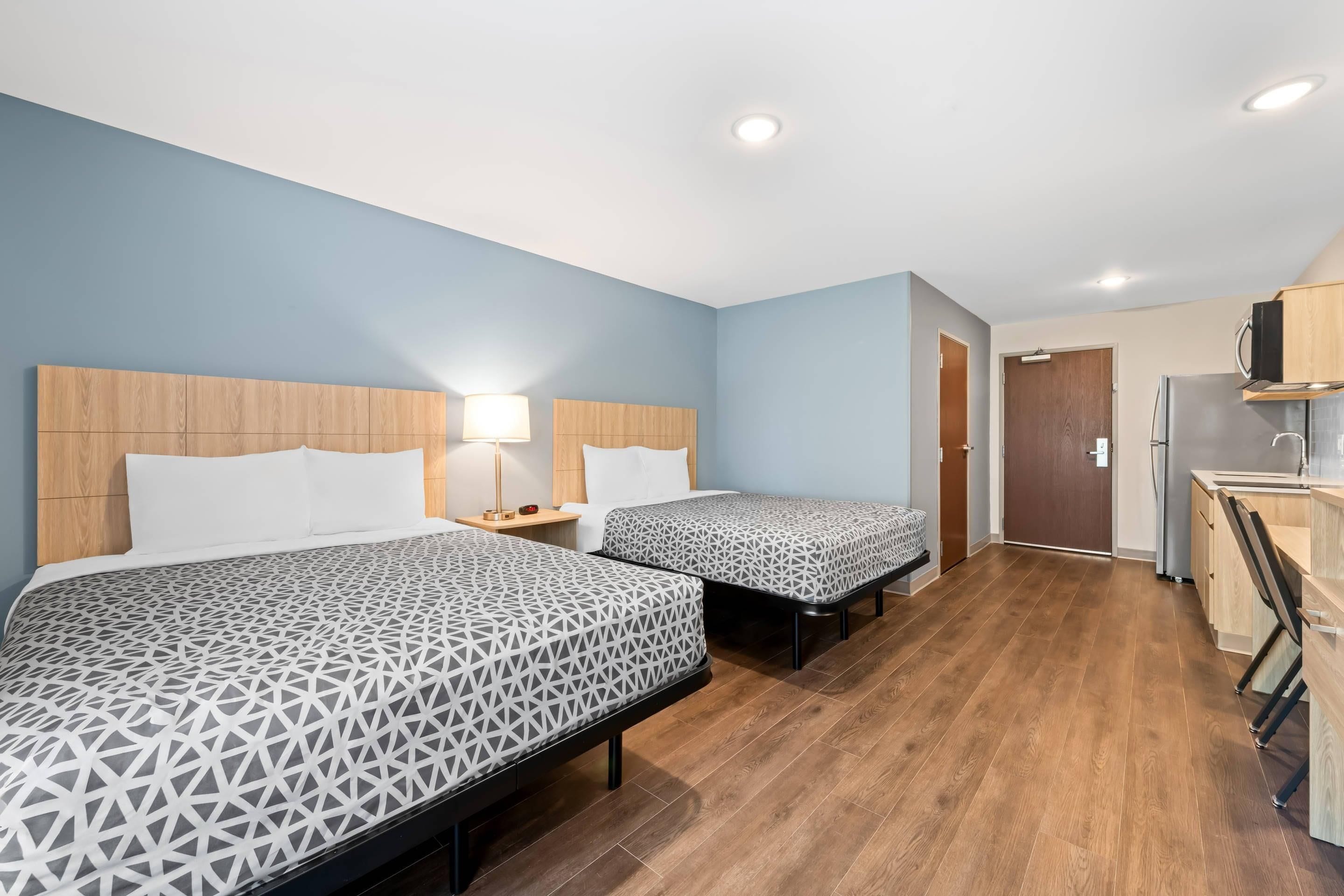 A hotel room with two beds, a kitchenette, and a bathroom.