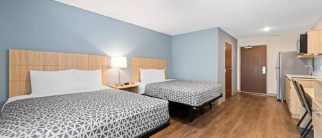 A hotel room with two beds, a kitchenette, and a bathroom.