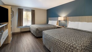 Een hotelkamer met twee bedden, een televisie, een bureau met lades, een raam met gordijnen en een lampje op het nachtkastje.