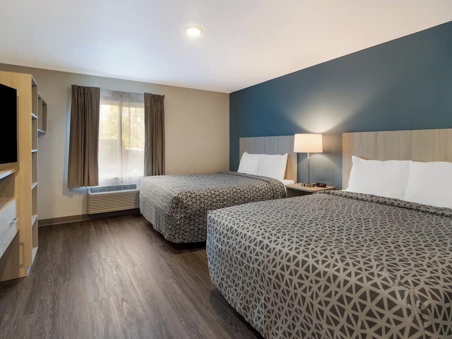 Une chambre d’hôtel avec deux lits, une télévision, un bureau avec des tiroirs, une fenêtre avec des rideaux et une lampe sur la table de chevet.
