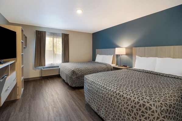 Une chambre d’hôtel avec deux lits, une télévision, un bureau avec des tiroirs, une fenêtre avec des rideaux et une lampe sur la table de chevet.