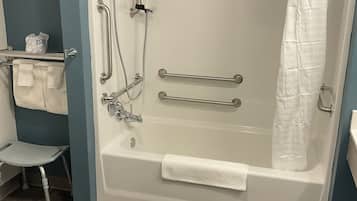 Een douche met lage drempel, grepen, een handdouche en een wit douchegordijn.