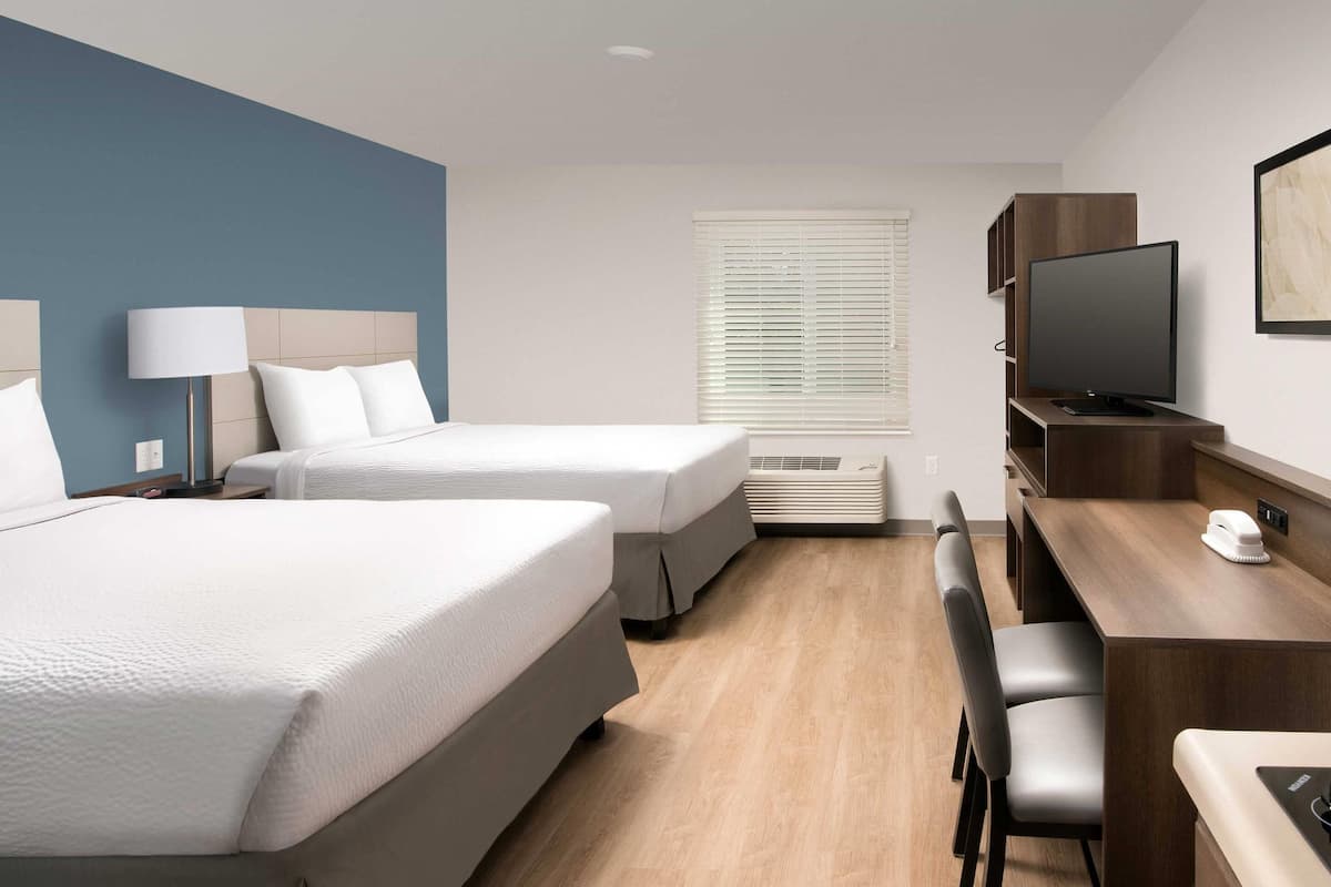 Une chambre d’hôtel avec deux lits, un bureau avec une chaise, une télévision et une fenêtre avec des stores.
