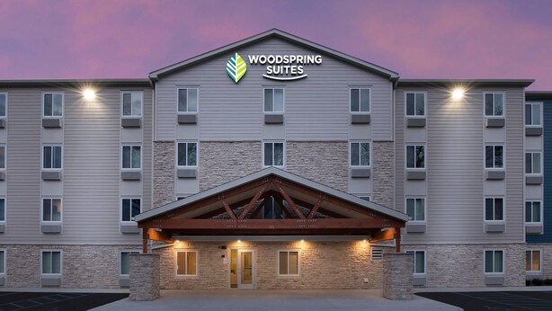 Een hotel met meerdere verdiepingen, een gevel van steen en een opvallend bord met 'Woodspring Suites'.