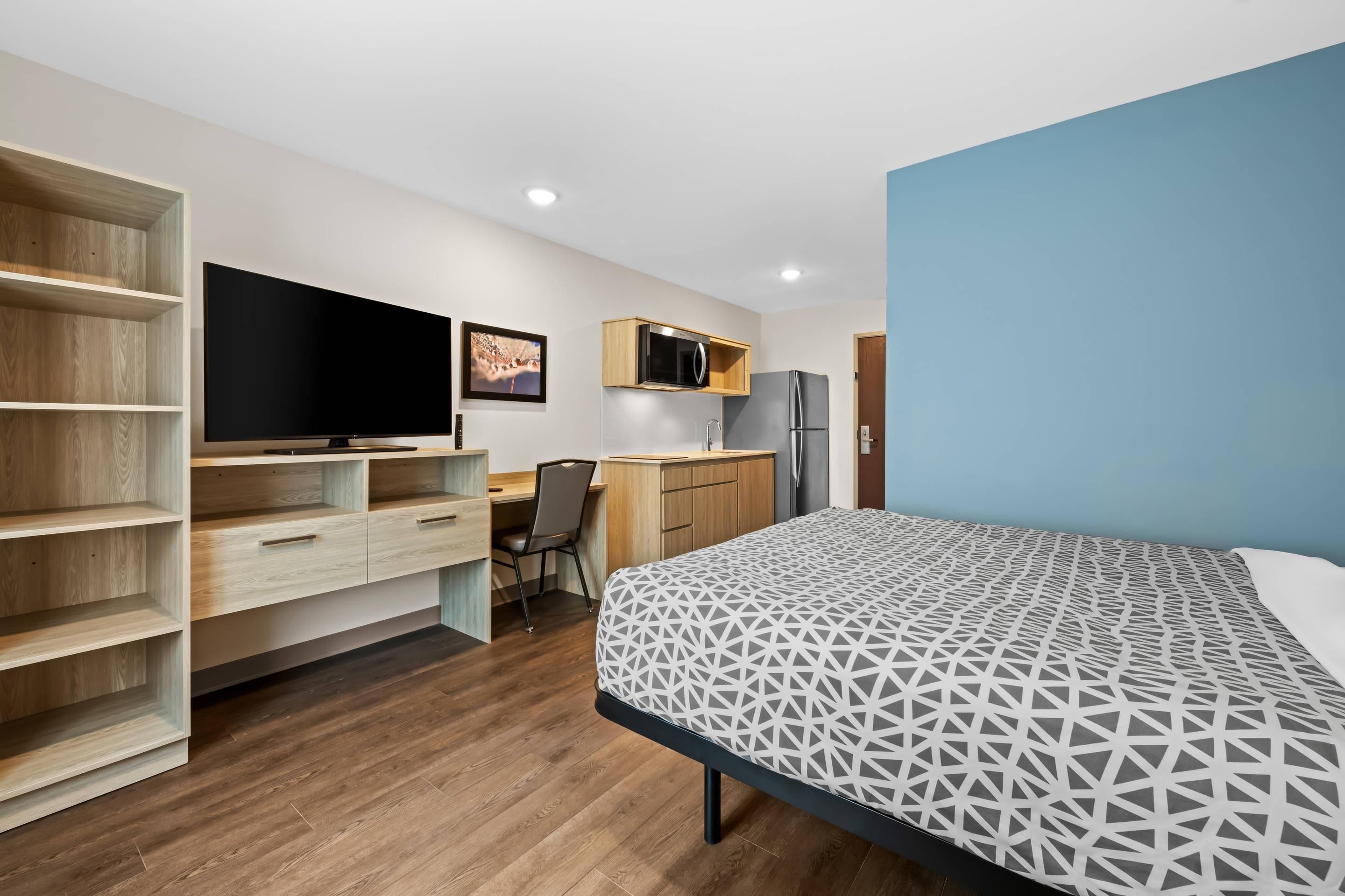 A compact room with a bed, a desk, a chair, a TV, a microwave, and a refrigerator.
