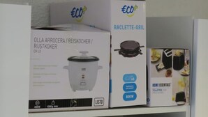 Un electrodoméstico, una parrilla para raclette y un folleto en un estante.
