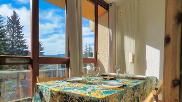 Un comedor con una mesa dispuesta para cuatro personas, ventanas amplias y vistas a árboles y montañas.