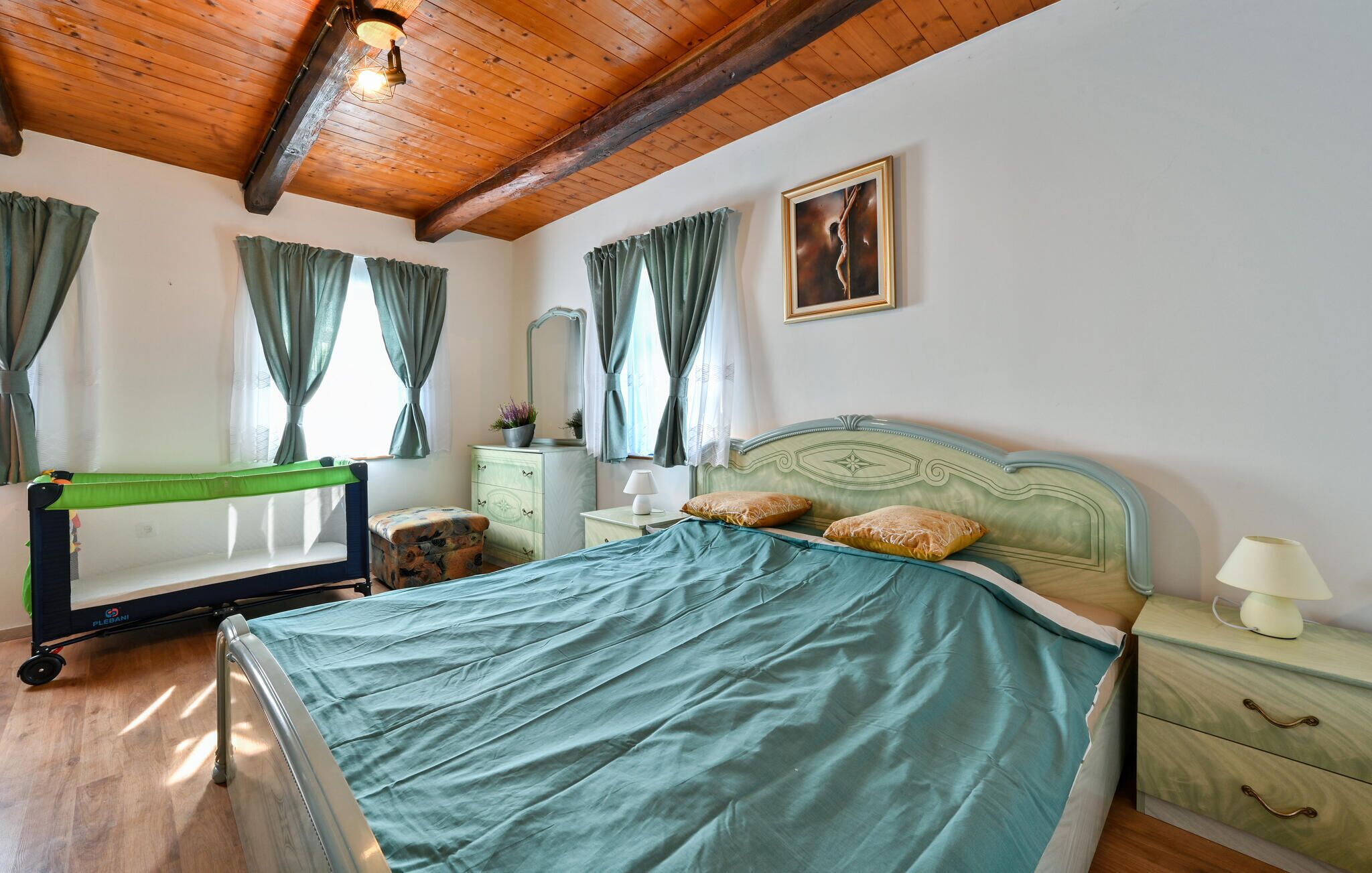 Une chambre à coucher comprenant un lit, une table de chevet, une commode, un miroir et une fenêtre avec des rideaux.
