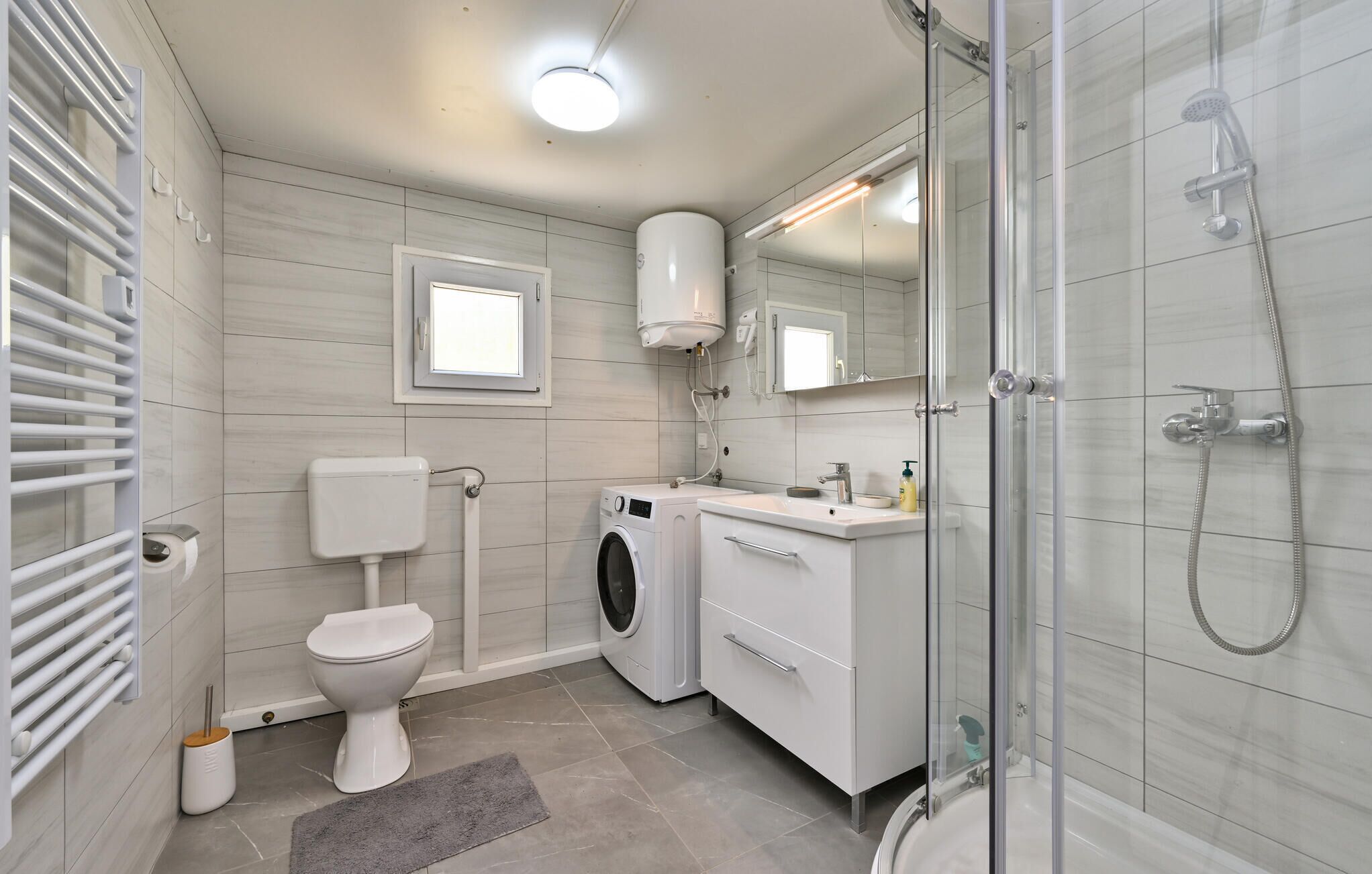 A modern bathroom with a toilet, washing machine, sink, and shower.