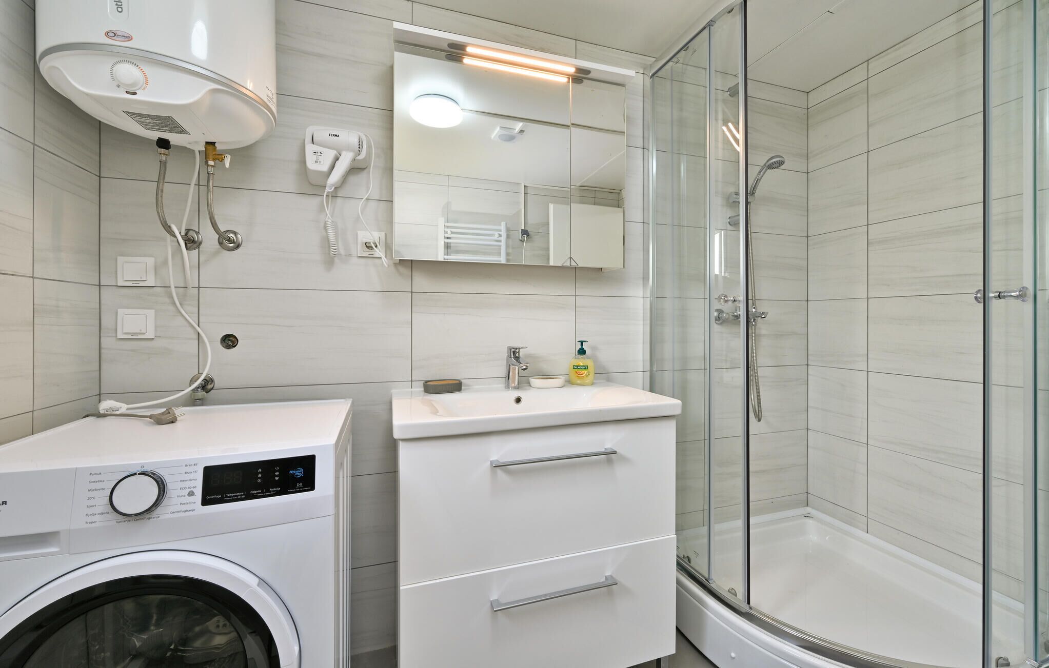 A modern bathroom with a washing machine, a sink, and a glass-enclosed shower.