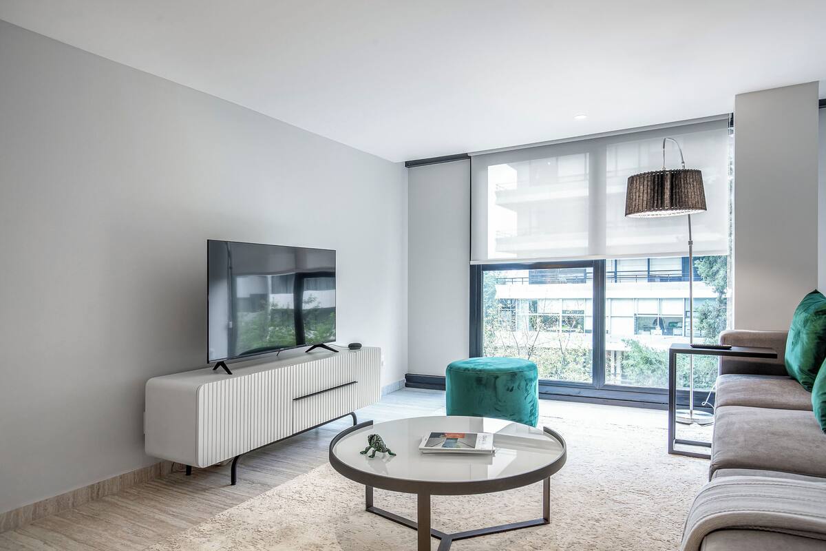 Ein modernes Wohnzimmer mit Fernseher, Sofa und rundem Couchtisch.