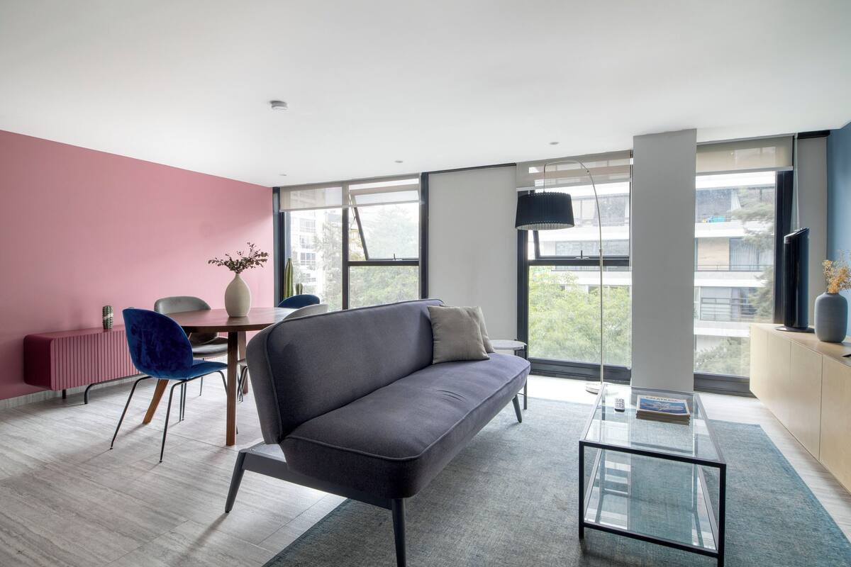Ein modernes Wohnzimmer mit grauem Sofa, einem Glastisch und einer Wand in Rosa.
