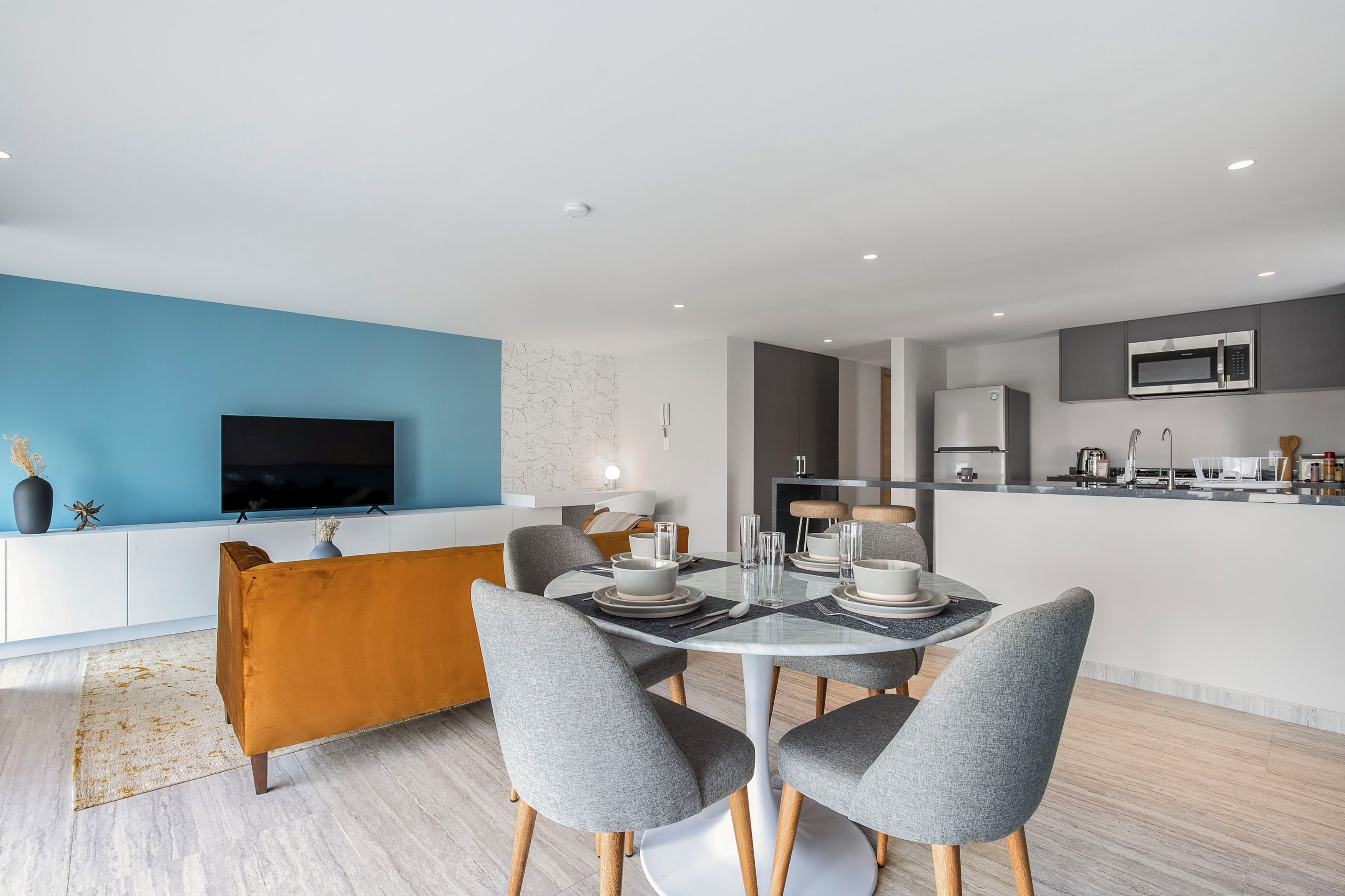 Una sala de estar moderna con comedor, cocina y televisor montado en la pared.