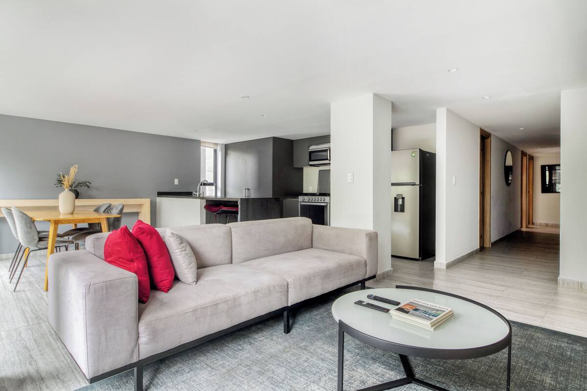Ein modernes Wohnzimmer mit einer Couch, einem Esstisch und einer Küche im Hintergrund.