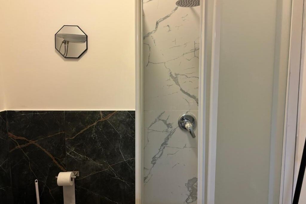 A bathroom with a marble wall, a shower enclosure, and a toilet paper holder.