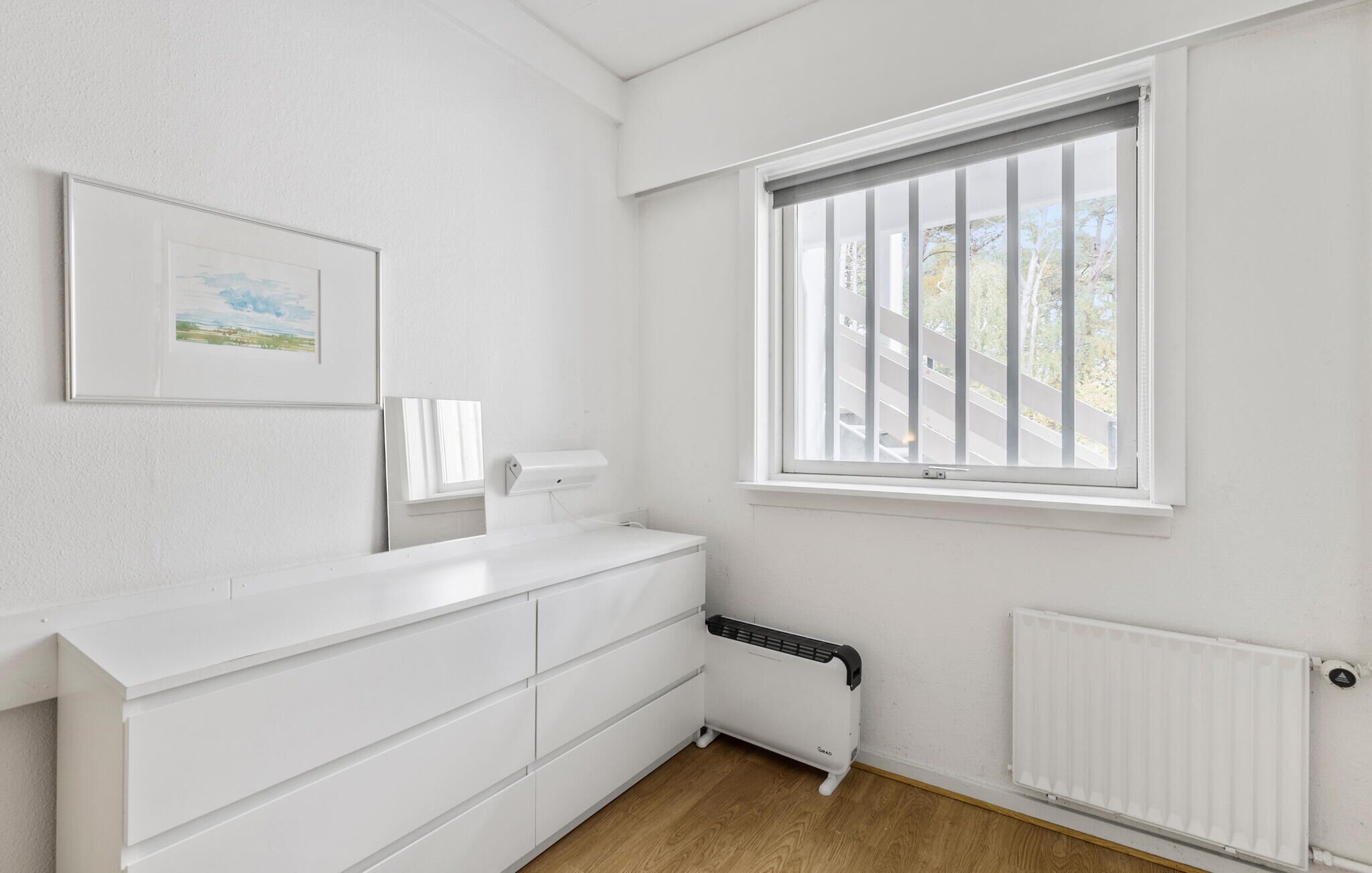 Ein heller Raum mit großem Fenster, Heizkörper und weißem Schrank.