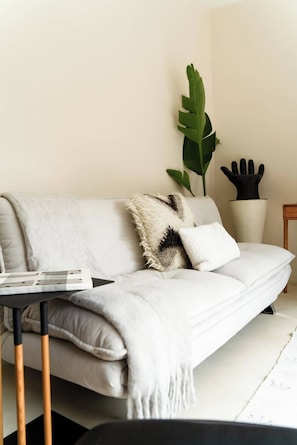 A modern living room with a white sofa, a black coffee table, and a large green plant.