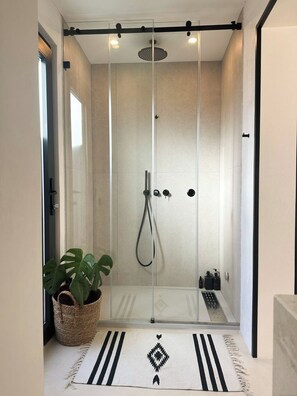 Box doccia moderno con porta in vetro, soffione a soffitto e doccetta manuale.