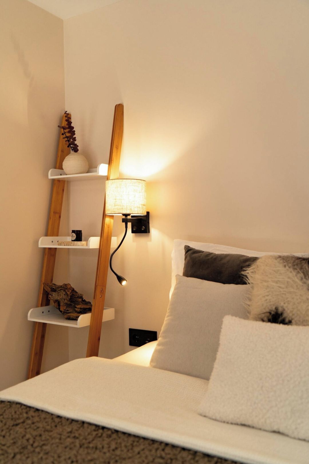 A bedroom with a bed, a bedside lamp, and a wooden shelf unit with decorative items.