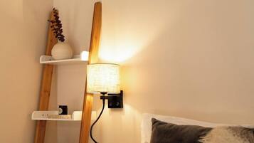 A bedroom with a bed, a bedside lamp, and a wooden shelf unit with decorative items.