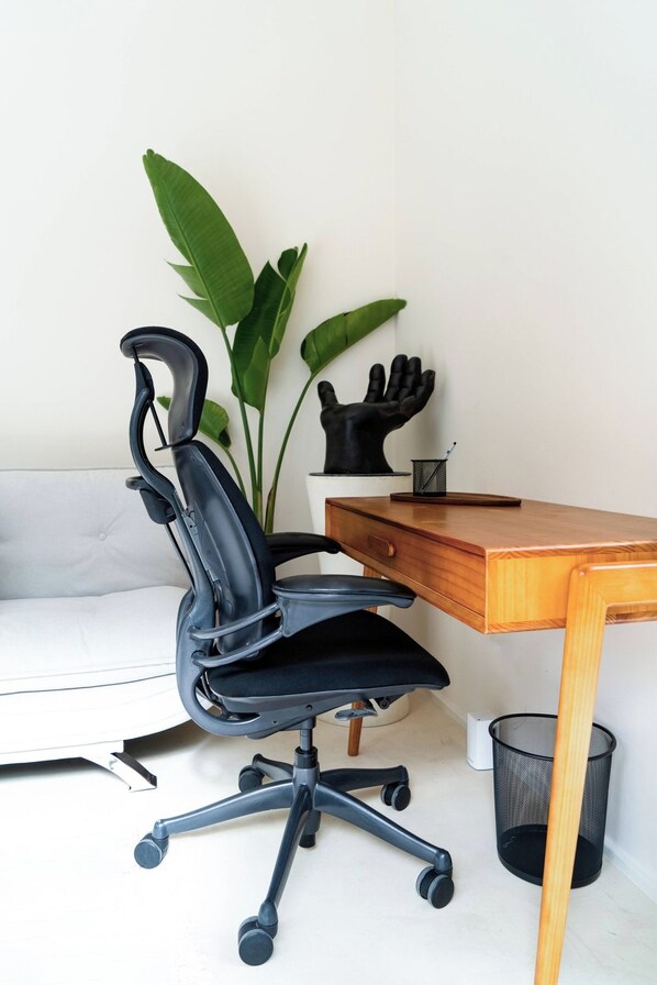 A black office chair with a high backrest and armrests, positioned next to a wooden desk with a drawer.