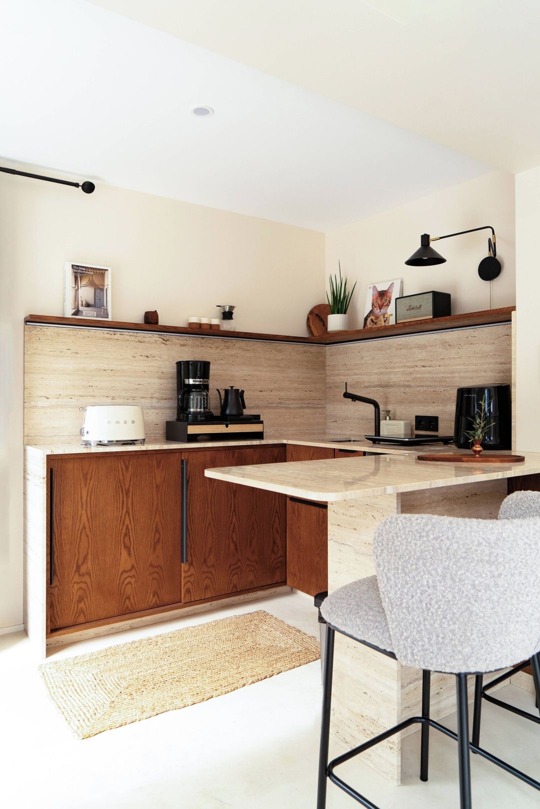 A modern kitchen with a central island, wooden cabinets, a coffee machine, and a small dining area with a chair.