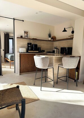 A modern kitchen with a central island, two bar stools, and a dining area with a woven table.