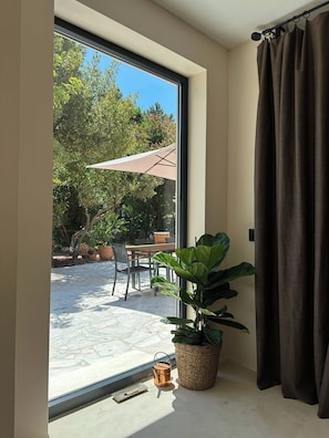 A room with a large window, a potted plant, a metal bucket, and a curtain.